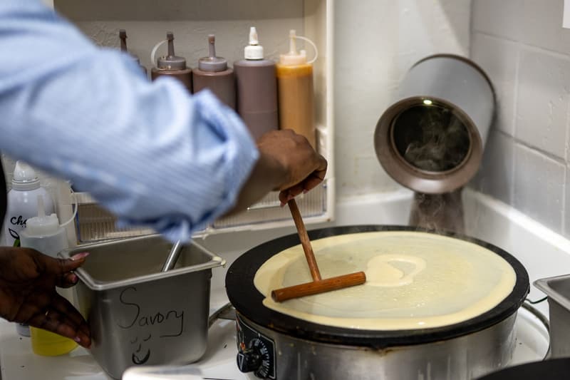 Spreading crepe batter across the hot round iron with a wooden spreader