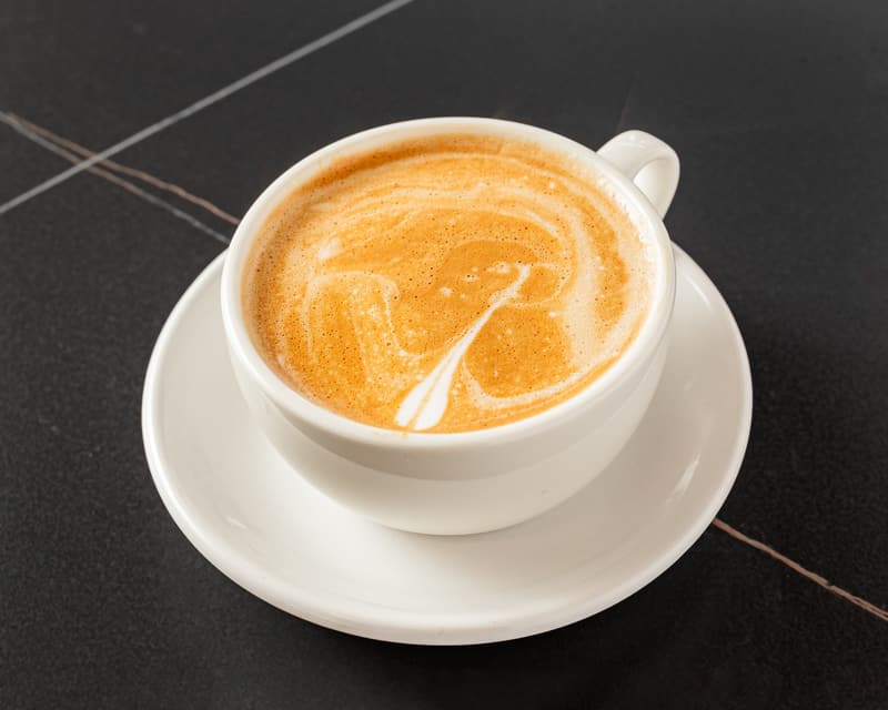 A cappuccino in a white cup on a saucer, with a leaf pattern in the foam