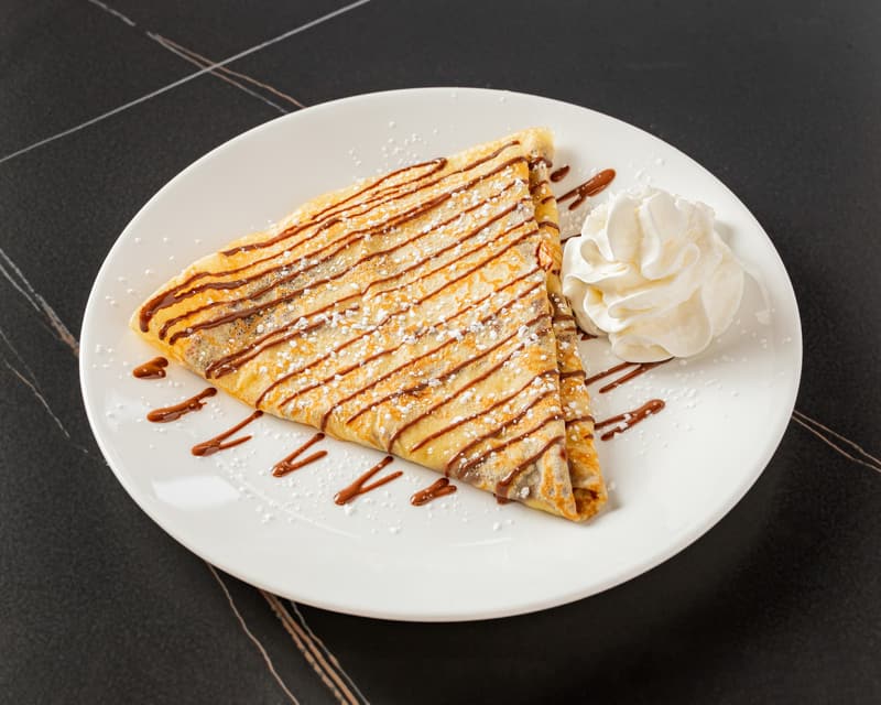 The Nutella Crêpe: a folded crepe with chocolate drizzle, powdered sugar, and whipped cream