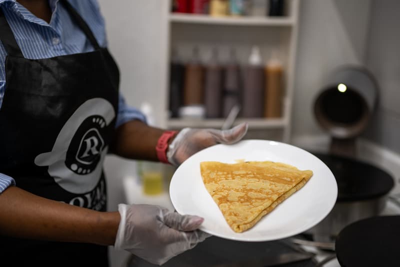 A folded crepe on a white plate, held by a team member in a 96 Royal apron at the crepe station