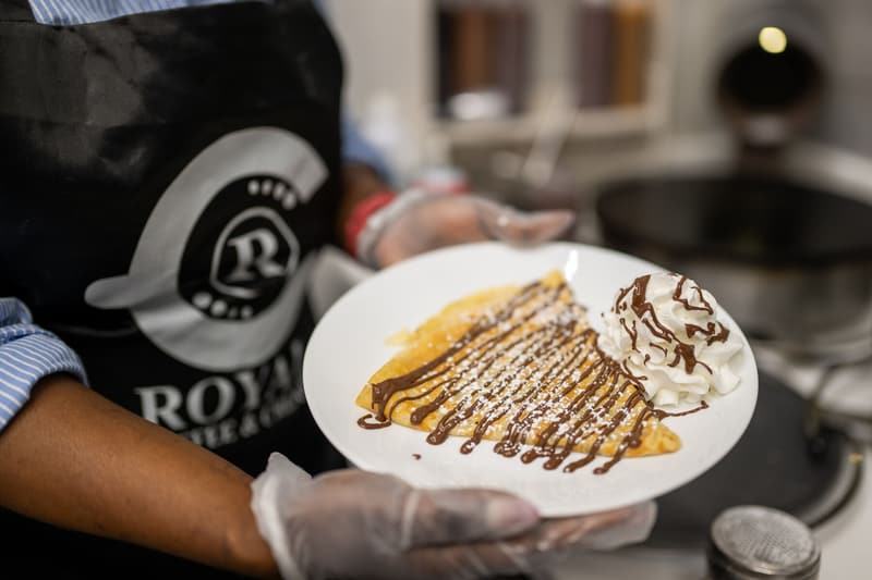 A crepe with chocolate drizzle, powdered sugar, and whipped cream, handed across the counter