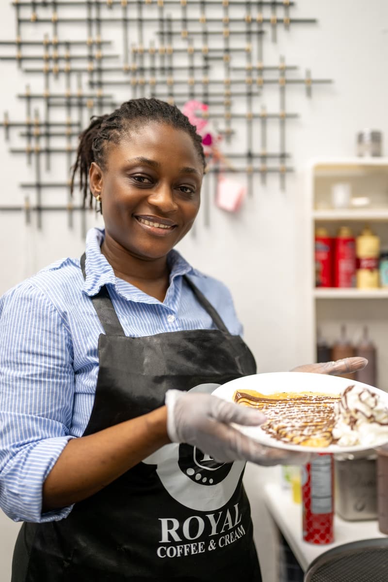 A team member in a 96 Royal apron holding out a plated crepe and smiling