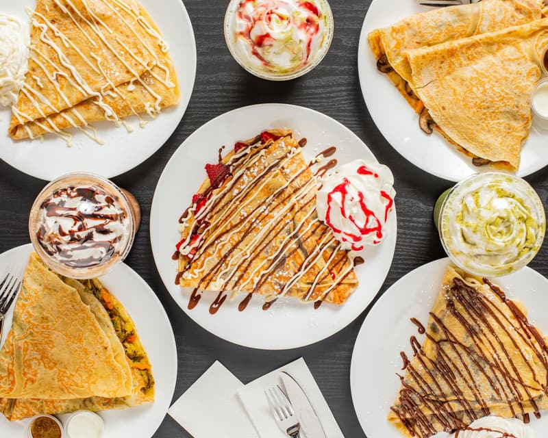 Seven crepes and three cold drinks on a dark table, seen from above