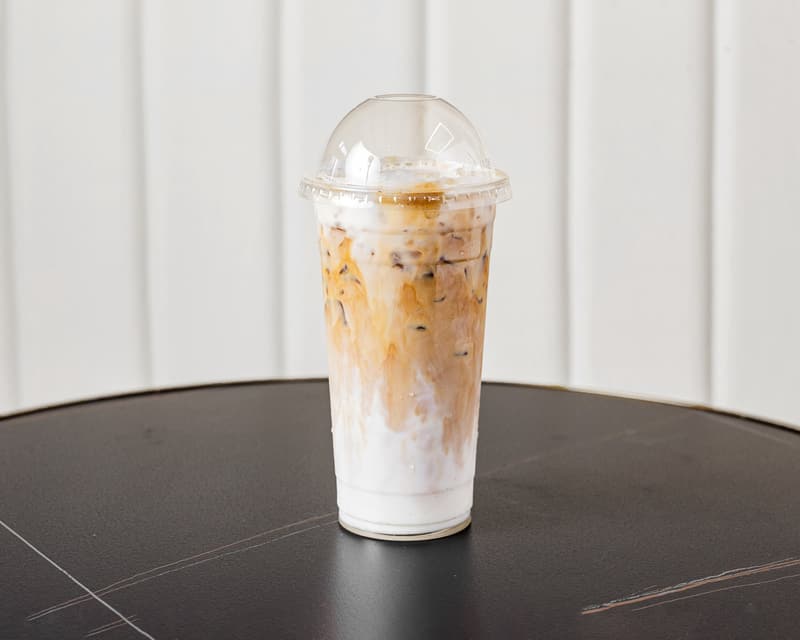 An iced latte in a tall clear cup on a dark table