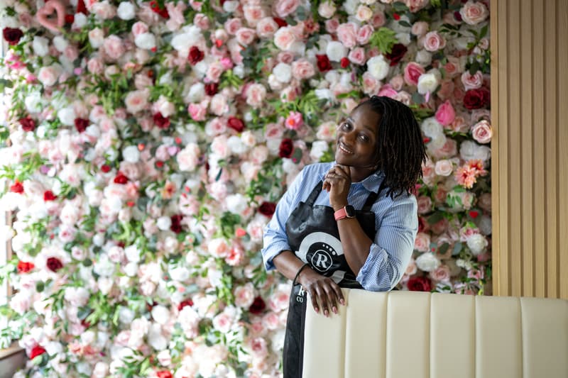 Yefon leaning on the banquette by the rose wall, chin in hand, smiling