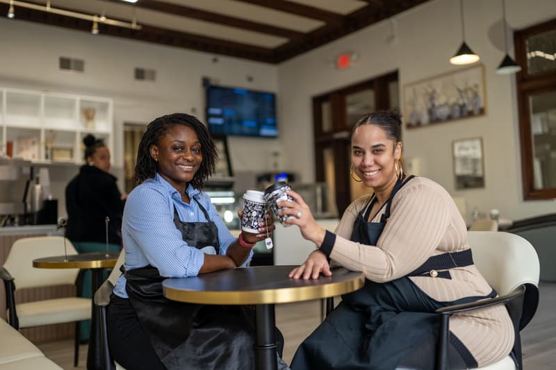 Yefon and a team member at a cafe table, raising 96 Royal cups toward each other and smiling